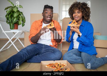 Junges schwarzes Paar macht Mittagspause mit Pizza am Umzugstag Stockfoto
