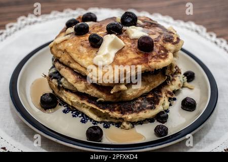 Ein Stapel Buttermilch-Blaubeerpfannkuchen mit Butter und Sirup für ein Frühstück auf einem Medaillon-Teller auf einer weißen Teigkuchen; Taylors Falls, Minnesota, USA. Stockfoto