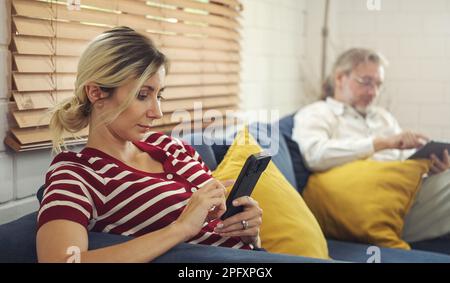 Gadgets Sucht. Vater und Tochter halten und benutzen verschiedene elektronische Geräte, während sie zu Hause auf dem Sofa sitzen. Stockfoto