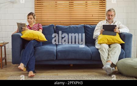 Gadgets Sucht. Vater und Tochter halten und benutzen verschiedene elektronische Geräte, während sie zu Hause auf dem Sofa sitzen. Stockfoto