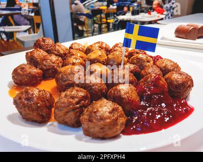 Frische leckere Fleischbällchen mit Cranberry-Sauce auf weißem Teller mit schwedischer Flagge. Stockfoto