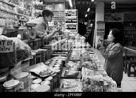 Eine vietnamesische Kundin mittleren Alters unterhält sich mit einer jungen Frau, die einen Verkaufsstand betreibt und lokale Spezialitäten im Dalat Market, Vietnam, verkauft. Stockfoto