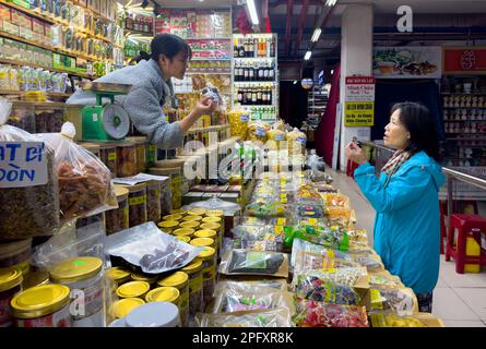 Eine vietnamesische Kundin mittleren Alters unterhält sich mit einer jungen Frau, die einen Verkaufsstand betreibt und lokale Spezialitäten im Dalat Market, Vietnam, verkauft. Stockfoto