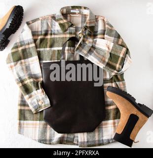 Schwarze umweltfreundliche Einkaufstasche mit Platz für Text. Bag-Modell-Vorlage, Draufsicht. Kleiderschrank mit Hemd und Stiefeln. Kleidung und Accessoires. Moderne Accessoires. Unisex-Karohemd Stockfoto