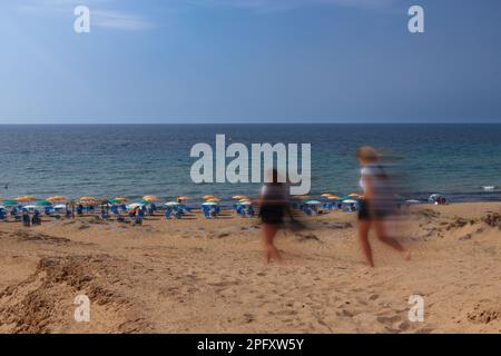 Touristen, die am Strand spazieren, gefangen in Bewegung, Sandstrand auf der Insel Korfu Stockfoto