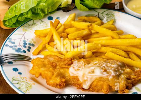 Portion von köstlichem hausgemachtem gemahlenem Fisch und frittiertem fisch mit Metallgabel in weißem Keramikgericht. Frisches grünes Gemüse und eine Tasse hausgemachte Sauce Stockfoto
