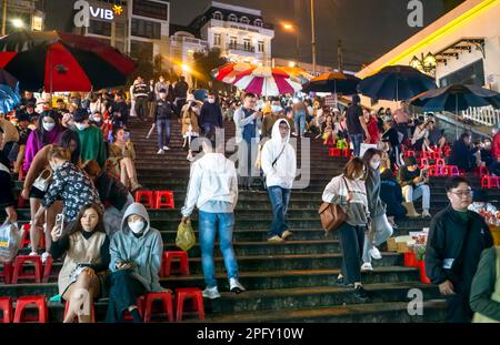 Junge Vietnamesen treffen sich mit Freunden, um auf Treppen mit Blick auf den Nachtmarkt in Dalat, Vietnam, zu sitzen. Stockfoto