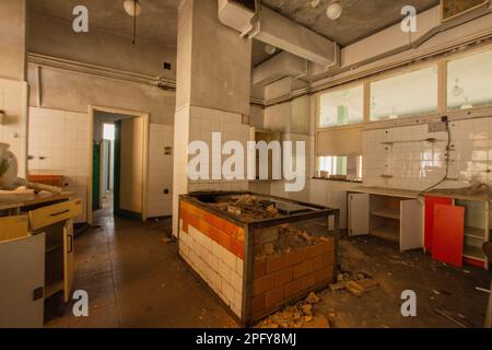 Das Innere einer verlassenen Industrieküche voller Müll, Möbeln und Gläsern, die von den Benutzern hinterlassen wurden. Stockfoto