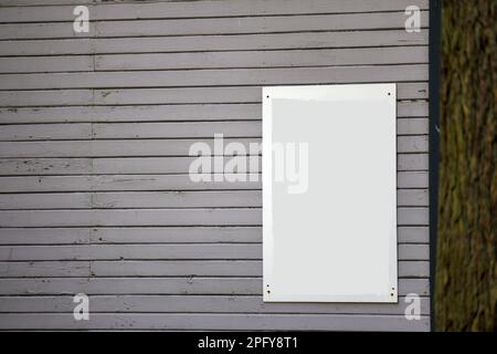 Eine bemalte Holzplankenwand in hellgrau-brauner Farbe mit einer hellen Tafel Stockfoto