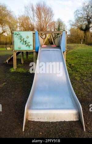 Silberne Edelstahlrutsche, die von der hölzernen Spielstruktur auf dem Kinderspielplatz kommt. Stockfoto