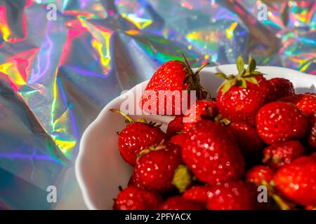 Erdbeerfest. Nahaufnahme einer gekürzten Schüssel reifer roter Erdbeeren auf modernem Hologramm-Hintergrund. Obst und Beeren. Ernte- und Erntegutkonzept. Orgel Stockfoto