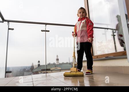 Mädchen im Vorschulalter putzt Balkonboden mit Mopp. Frühjahrsputz-Konzept Stockfoto