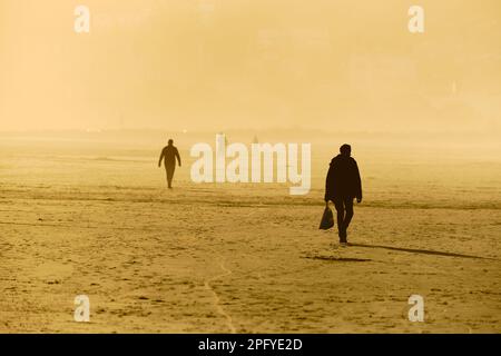 Menschen, die während der goldenen Stunde am Strand entlang spazieren, Bilder, die durch Sonnenlicht golden und Silhouetten gegen das Licht Stockfoto