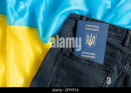 Ein ausländischer biometrischer ukrainischer Reisepass liegt in einer Jeanstasche vor dem Hintergrund der ukrainischen Flagge Stockfoto