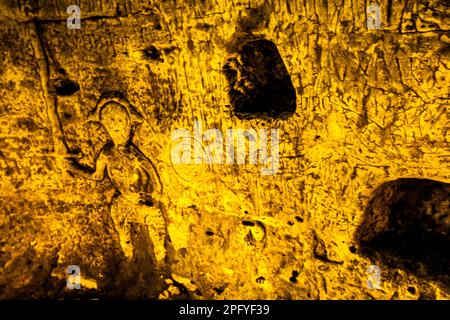 Die Royston Cave in Herfordshire, Großbritannien, verwirrt heute noch Historiker. Die Höhle ist mit einer großen Anzahl von Wandskulpturen mit niedrigem Relief dekoriert. Es sind hauptsächlich christliche Motive im mittelalterlichen Stil. Die Figur mit dem gezogenen Würm könnte den Heiligen Michael oder vielleicht den Heiligen Georg repräsentieren, der später Schutzpatron von England war. Der Würfel der Figur zeigt auf das, was Jasus und die zwölf Jünger mit Judas zu sein scheinen, die kleine Figur hinten am rechten Ende der Reihe. Royston Cave in Katherine's Yard, Melbourn Street, Royston, England Stockfoto