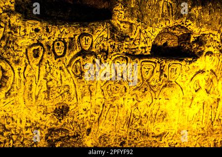 Die Royston Cave in Herfordshire, Großbritannien, verwirrt heute noch Historiker. Die Höhle ist mit einer großen Anzahl von Wandskulpturen mit niedrigem Relief dekoriert. Es sind hauptsächlich christliche Motive im mittelalterlichen Stil. Oben links ist eine Kreuzigung dargestellt. Royston Cave in Katherine's Yard, Melbourn Street, Royston, England Stockfoto