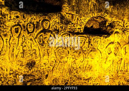 Die Royston Cave in Herfordshire, Großbritannien, verwirrt heute noch Historiker. Die Höhle ist mit einer großen Anzahl von Wandskulpturen mit niedrigem Relief dekoriert. Es sind hauptsächlich christliche Motive im mittelalterlichen Stil. Oben links ist eine Kreuzigung dargestellt. Royston Cave in Katherine's Yard, Melbourn Street, Royston, England Stockfoto