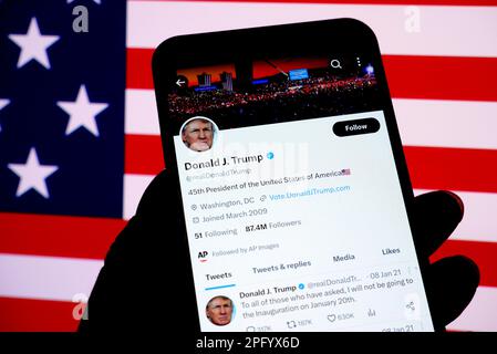 In dieser Fotoabbildung wird ein Twitter-Konto des ehemaligen US-Präsidenten Donald Trump auf einem Smartphone mit einer amerikanischen Flagge im Hintergrund angezeigt. Stockfoto