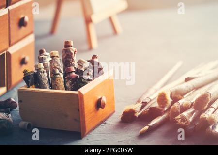 Künstlerische Ausrüstung in einem Künstlerstudio: Alte gebrauchte Farbröhren in einer Holzkiste, gebrauchte künstlerische Pinsel zum Malen mit Öl- oder Acrylfarben; Stockfoto