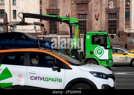 Moskau, Russland. 19. März 2023. Ein städtischer Abschleppwagen und ein Citydrive Carsharing Service Car fahren auf einer Straße im Zentrum von Moskau, Russland Stockfoto