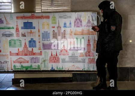 Moskau, Russland. 19. März 2023. Ein Wachmann steht an einem Zaun mit Bildern der Gebäude der Stadt Moskau in der Unterführung im Stadtzentrum von Russland Stockfoto