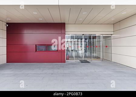 Eingangstor zu einem Bürogebäude mit einer roten Wand kombiniert mit anderen cremefarbenen Wänden und Zugangstüren mit roten Punkten an den Fenstern Stockfoto