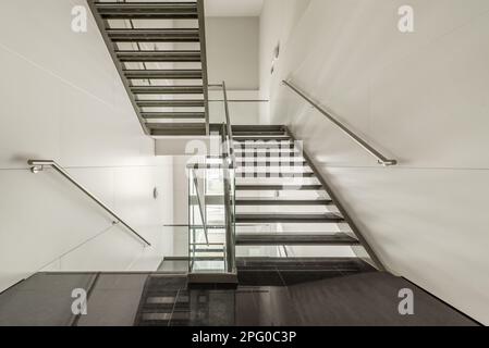 Leicht gestaltete Treppen aus Edelstahl, gehärtetem Glas und Stufen aus poliertem schwarzem Granit in einem Bürogebäude Stockfoto