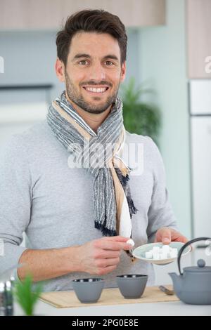 Ein lächelnder Mann gibt zu Hause Zucker in Teetassen Stockfoto