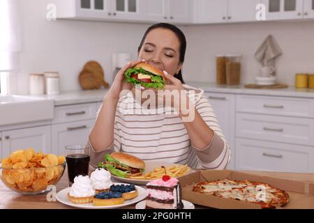 Übergewichtige Frau, die zu Hause Burger isst Stockfoto