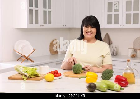 Schöne übergewichtige Frau, die eine gesunde Mahlzeit am Tisch in der Küche zubereitet Stockfoto