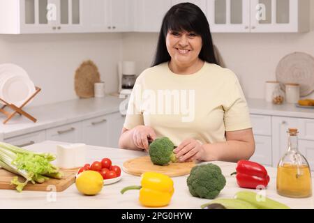 Schöne übergewichtige Frau, die eine gesunde Mahlzeit am Tisch in der Küche zubereitet Stockfoto