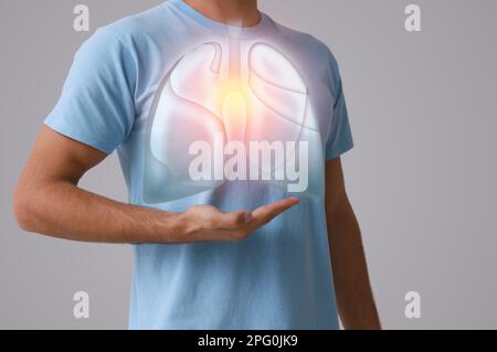 Ein Mann, der die Hand nahe der Brust hält, mit einer Darstellung der Lungen auf grauem Hintergrund, Nahaufnahme Stockfoto