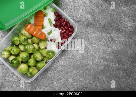 Schmackhafter Reis mit Schnitzeln und Gemüse in Kunststoffbehälter auf grauem Tisch, Draufsicht. Platz für Text Stockfoto