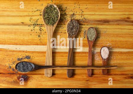 Chia, Kreuzkümmel, Pfeffer, Mohnsamen, rosa Salz auf Holzlöffeln und natürlicher Holzboden Stockfoto