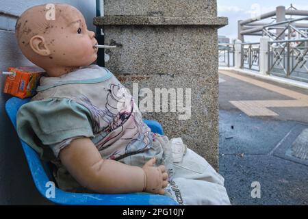 Am Phra Arthit Pier am Chao Phraya River, Bangkok, Thailand, hat jemand die Puppe eines Jungen auf einen Stuhl gelegt und ihm eine Zigarette in den Mund gesteckt Stockfoto