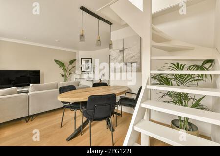 Ein Wohnzimmer mit weißen Wänden und Holzfußboden, einschließlich einem runden Esstisch umgeben von zwei schwarzen Stühlen Stockfoto