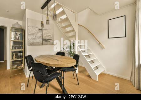 Ein Speisesaal mit einem Holztisch und schwarzen Stühlen vor einer Treppe, die in die zweite Etage führt Stockfoto