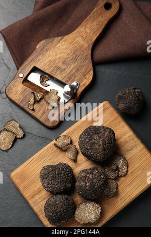 Holzrasierer mit ganzen und geschnittenen Trüffeln auf schwarzem Tisch, flach liegend Stockfoto