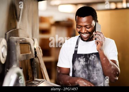 Ich werde Ihr Mittagessen mit einer frischen Lieferung zu etwas ganz Besonderem machen. Ein männlicher Bäcker, der während der Arbeit sein Handy benutzt. Stockfoto