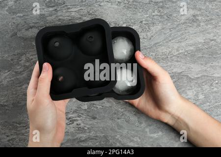 Eine Frau, die Schimmel mit gefrorenen Eisbällen am grauen Tisch hält, Draufsicht Stockfoto