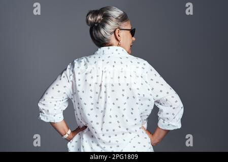 Sie ist die coolste Ladung im ganzen Block. Rückansicht einer Seniorin, die eine Sonnenbrille trägt, während sie vor grauem Hintergrund posiert. Stockfoto