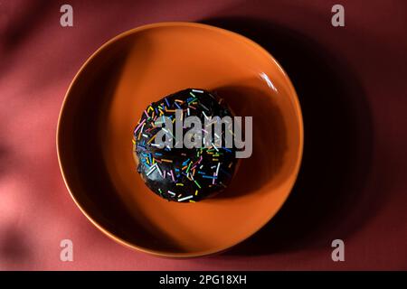 Bunte Donuts in orangefarbener Platte auf rotem Hintergrund. Draufsicht Stockfoto