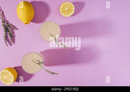 Lavendel-Limonade und Zitronen auf violettem Hintergrund mit langen Schatten, Draufsicht Stockfoto