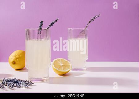 Zwei gerippte Gläser mit Lavendel-Limonade auf violettem Hintergrund, erfrischendes Sommergetränk Stockfoto