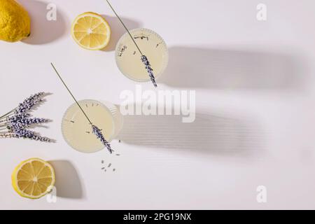 Stillleben mit Lavendel-Limonade und Zitronen auf dem weißen Tisch mit langen Schatten, Draufsicht Stockfoto
