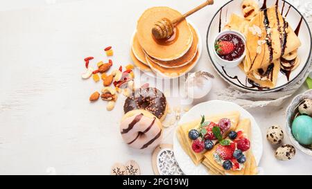 Süßer Ostertisch. Pfannkuchen, Crepes, Waffeln und Donuts mit frischen Beeren, Nüssen und Belag. Ostern traditionelle, natürliche bunte Eier. Bis Stockfoto