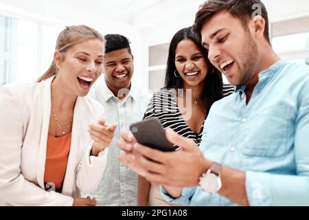 Sehen Sie sich das an. Ein gutaussehender junger Geschäftsmann, der seinen Kollegen etwas Lustiges auf seinem Handy zeigt. Stockfoto