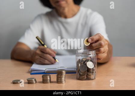 Frau spart Geld durch das Einlegen von Münzen in Glas, Finanz- und Buchhaltungskonzept. Stockfoto