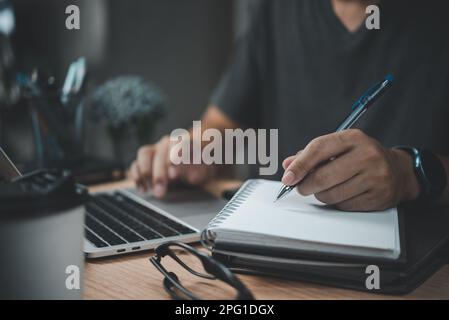 Ein Mann schreibt mit einem Stift auf einem Notizbuch im Büro. Lernen, Bildung und Arbeit. Schreibt Ziele, Pläne, To-do und Wunschliste auf dem Schreibtisch. Stockfoto
