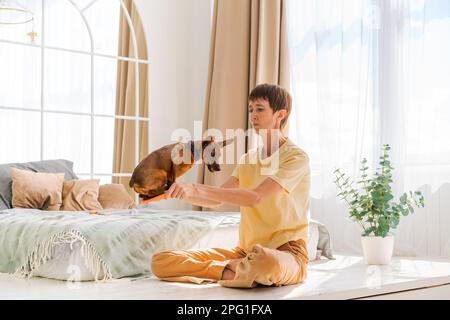 Besitzer spielt mit fröhlichem Hund zu Hause, glückliche reife Frau genießt Sport mit ihrem süßen Miniaturpinscher. Mit dem Konzept eines Hundes zu Hause im Schlafzimmer auf dem Bett zu spielen Stockfoto